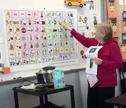 photo of teacher pointing to a symbol on a poster-size Universal Core vocabulary display on the wall.