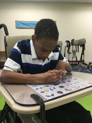 A student looking over the 30 location universal core board that is taped to the tray of his wheel chair.