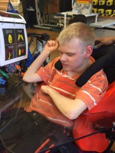 A high contrast 4 square communication book is mounted at eye level on a student's wheel chair.